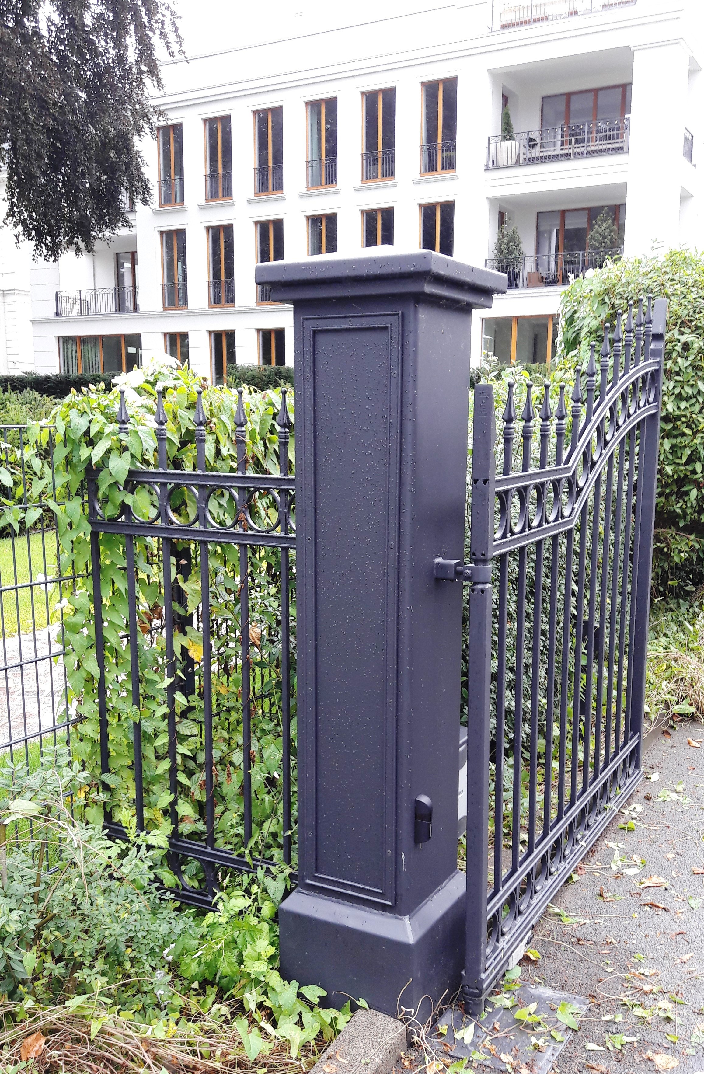 Schwarze Metalltoreinfahrt mit einem hohen, rechteckigen Torpfosten und einem...