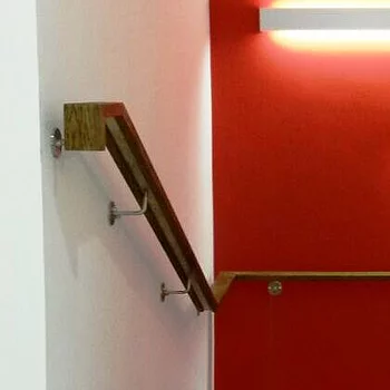 Holzhandlauf an einer Treppe mit Metallstützen, vor einer roten Wand.