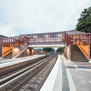 Eine moderne Brücke aus Stahl und Ziegel mit großen Fenstern, die über Gleise führt.