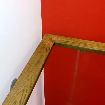 Holzhandlauf in L-Form an einer Wand, die rot gestrichen ist. 