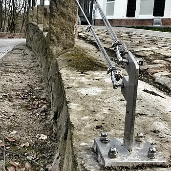 Zwei Stahlseile sind an einer Steinmauer befestigt, die zu einem modernen Gebäude führt.