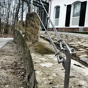 Zwei Stahlseile sind an einer Steinmauer befestigt, die zu einem modernen Gebäude führt.