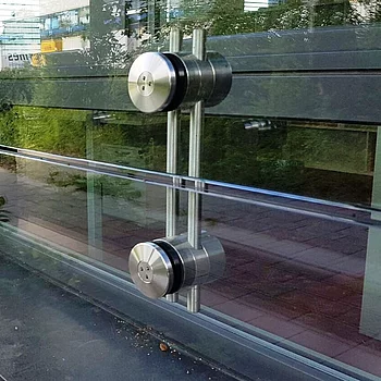 Zwei silberne Stahlbau-Befestigungen an einer Glaswand, mit runden, schwarzen Gummiringen...