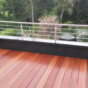 Holzterrasse mit vertikaler Metallgeländer und Blick auf einen Garten mit Bäumen und einem...