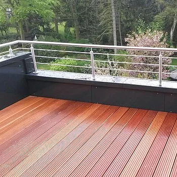 Holzterrasse mit vertikaler Metallgeländer und Blick auf einen Garten mit Bäumen und einem...